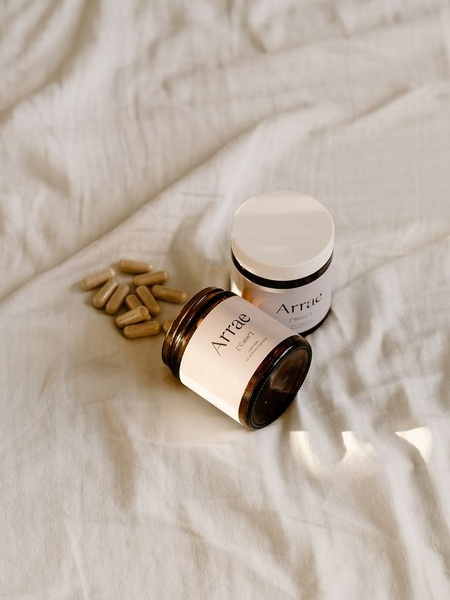 A high-end, soft-focus lifestyle image featuring two supplement jars and loose capsules arranged on textured fabric.
